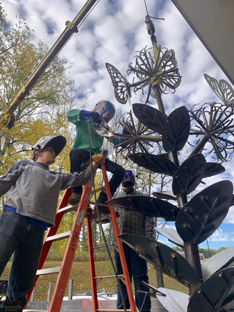 Alt Tag: Students welding a large butterfly and flower metal sculpture outdoors with guidance from Sam Castner