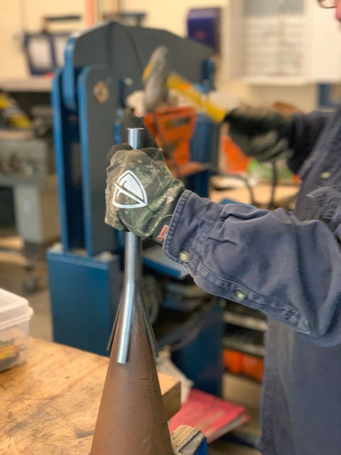 Close-up of a student shaping metal using a hammer and anvil as part of a sculpture project