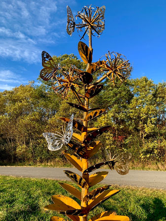 Completed butterfly and flower metal sculpture standing tall in a grassy outdoor space, designed by Sam Castner