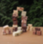 Colorful fudge squares stacked into a playful tower on a table, with a thuja tree in the background