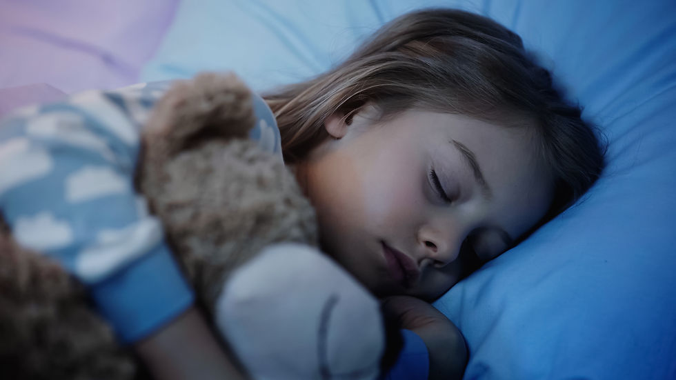 Sleeping child cuddles a teddy bear in a blue bed, peaceful and cozy in soft blue light.