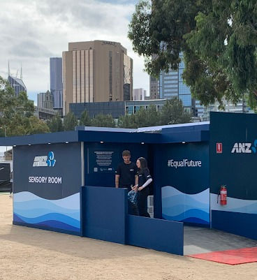 Exterior view of a small dark blue pop-up room with a sign 'Sensory Room' and with two people standing out the front