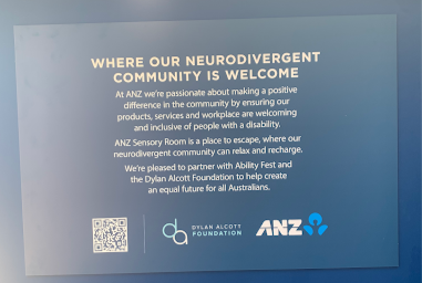 A sign on a dark blue background with branding and a QR code. Wording on the sign "Where our neurodivergent community is welcome. At ANZ we’re passionate about making a positive difference in the community by ensuring our products, services and workplace are welcoming and inclusive of people with a disability. ANZ Sensory Room is a place to escape, where our neurodivergent community can relax and recharge. We’re pleased to partner with Ability Fest and the Dylan Alcott Foundation to help create an equal future for all Australians."