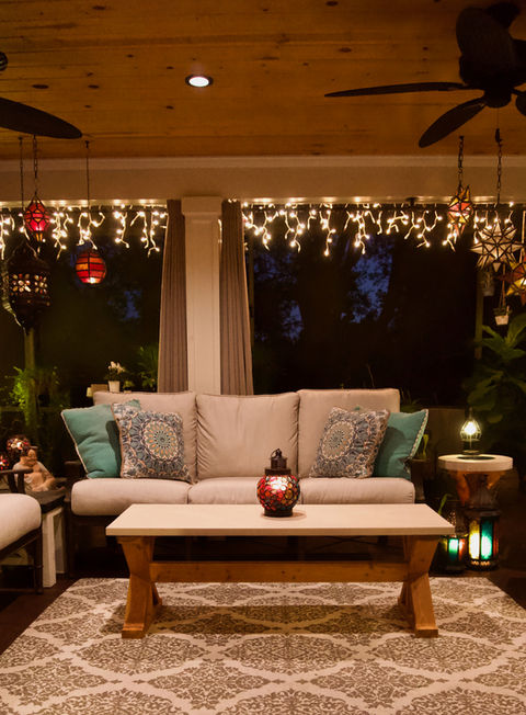 Covered lanai with a concrete coffee table, a concrete end table,  concrete planters, and tongue and groove pine ceiling at night with lit Moroccan lanterns, icicle lights, and potted plants in the background.
