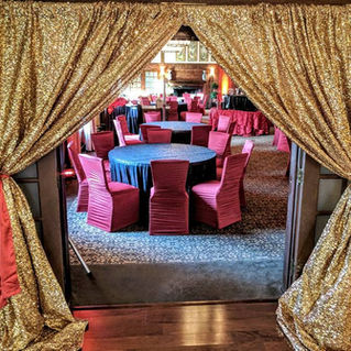 indoor country club wedding reception, holiday party work party with gold sequin drape swaged back with red satin sashes  for entrance to party with round tables, black tablecloth linens, and red chair covers on chairs 