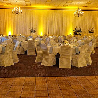indoor wedding reception with White Silk Pleated Ceiling Height Wall Drape, led uplighting, white rouge chair covers 