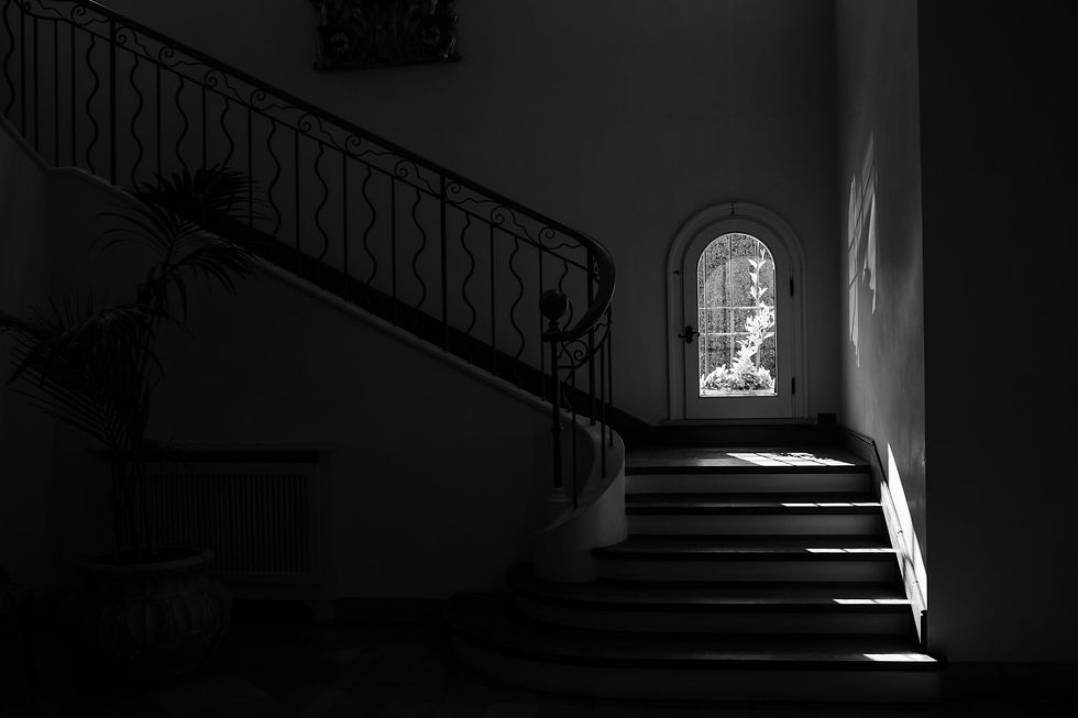 Fotografie di Drimage Creative studio di Simona Turano Photographer. Scala in penombra con ringhiera in ferro battuto e finestra ad arco, luce del sole filtra sui gradini, interno scuro e suggestivo con pianta in vaso.
