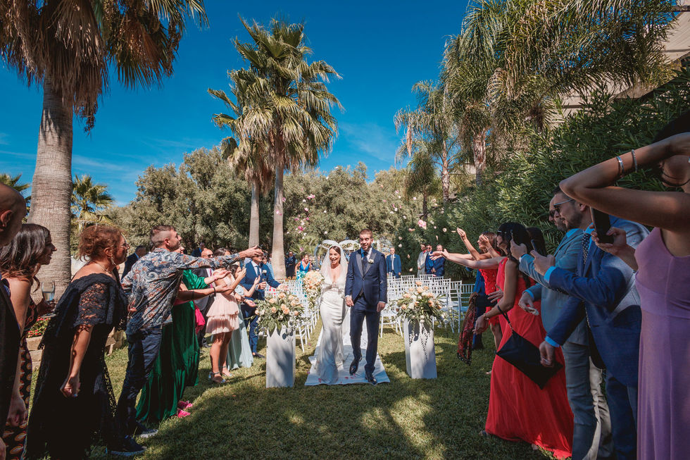 Sposi sorridenti camminano tra gli invitati dopo la cerimonia. Matrimonio verde-mare e gioia festosa.
