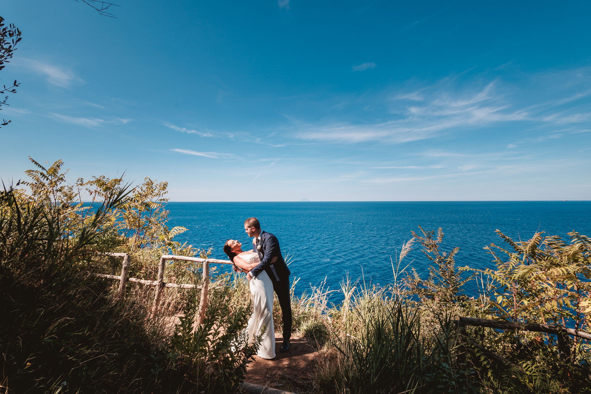 Una coppia balla con panorama marittimo; Matrimonio verde-mare in un giorno soleggiato.
