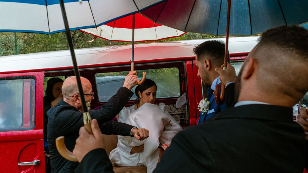 Bride exits vehicle as guests use umbrellas. E se piove… stiamo più freschi.
