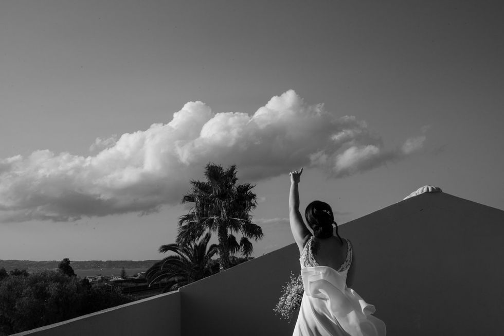 Donna in abito leggero alza braccio, cielo nuvoloso, autentiche emozioni.