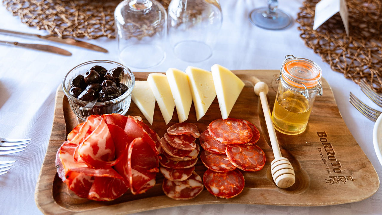 Wooden board with cheese, meat, olives, honey; restaurant table setting. Drimage