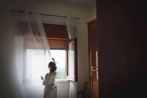 Sposa apre la finestra con tenda bianca, vista del paesaggio, Destination wedding in Calabria.