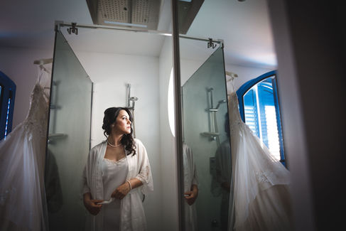 Bride in a white robe looks at her wedding dress in the mirror.