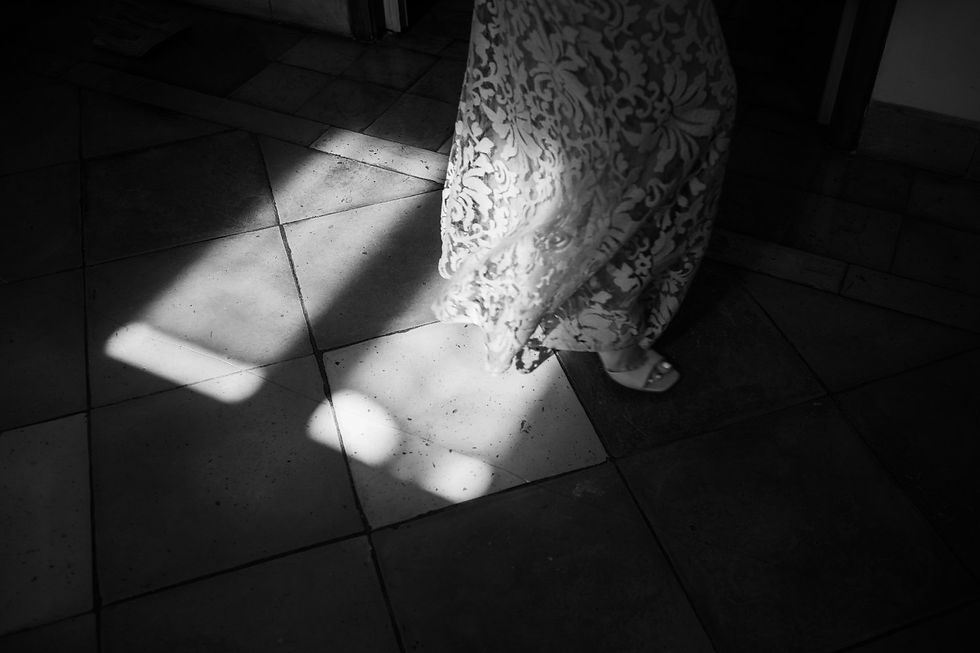 Fotografia di Drimage Creative studio di Simona Turano Photographer. Vista in bianco e nero di una persona con un abito a fantasia in piedi su un pavimento piastrellato illuminato dal sole, con giochi di luci e ombre molto suggestivi.