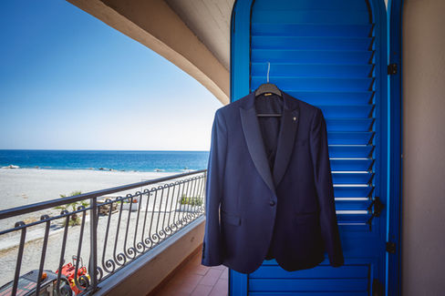Elegant navy suit jacket hangs from blue shutter overlooking ocean view.