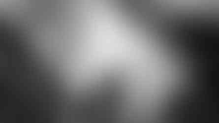 Newlyweds share a kiss below architecture in a black and white photo.