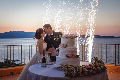 Coppia sposi si bacia, taglia torta nuziale con fuochi d'artificio, Matrimonio mare e monti.