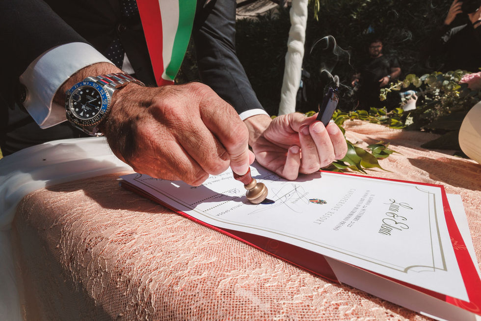Uomo firma documenti con sigillo. Matrimonio verde-mare durante cerimonia nuziale all'aperto. Drimage