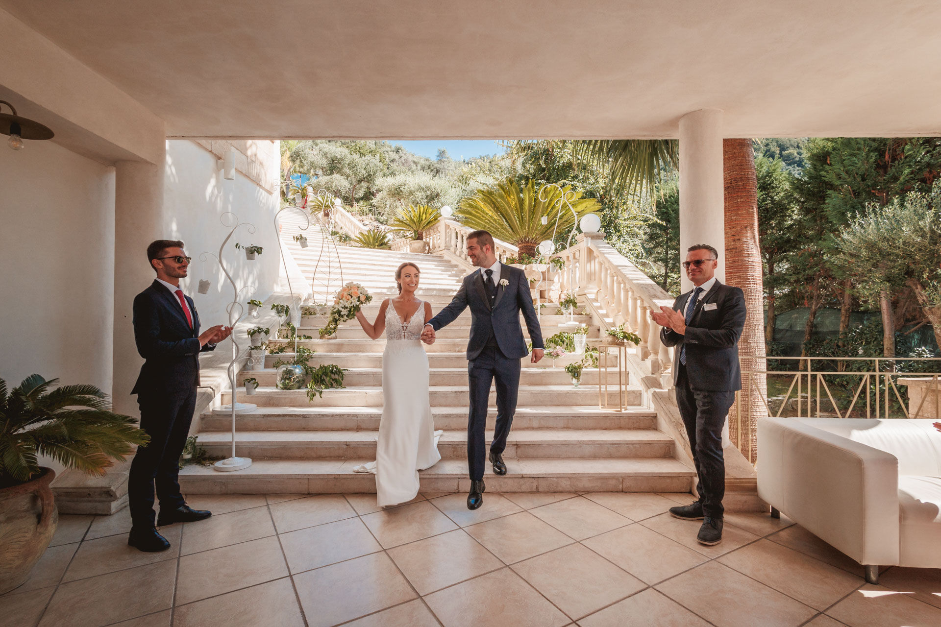Coppia sorridente scende le scale, Matrimonio verde-mare con testimoni maschi e fiori