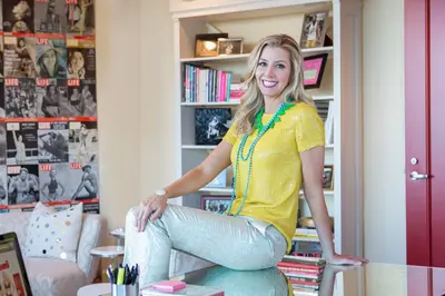 A business portrait of a creative founder seated on a desk in a vibrant, personality-filled office environment.