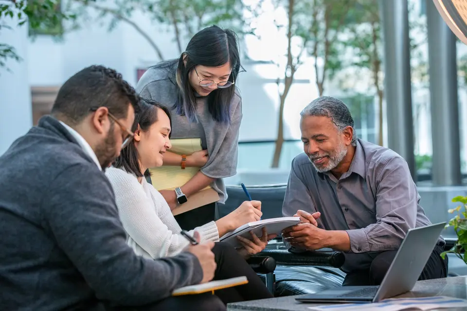 Coworkers collaborate in a bright lobby with natural light, representing open dialogue in corporate lifestyle spaces.