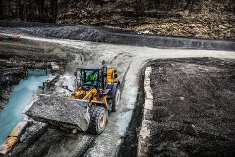 Drone photography near me of a bulldozer working beside a bright turquoise quarry water channel.
