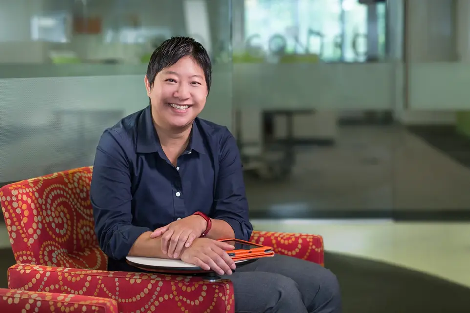 A business portrait of a smiling professional woman seated casually in a modern office lounge area.