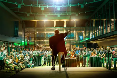 A speaker energizes a large company audience, demonstrating leadership in a dynamic corporate lifestyle event.