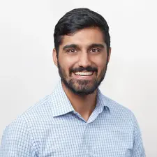 A man wearing a light blue checkered shirt smiling in a clean, well-lit portrait taken for corporate headshot photography services.