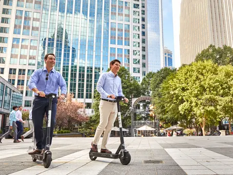 Two businessmen riding scooters in business plaza