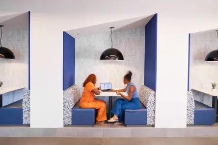 Two women collaborate in modern booth with laptop for lifestyle product photography.