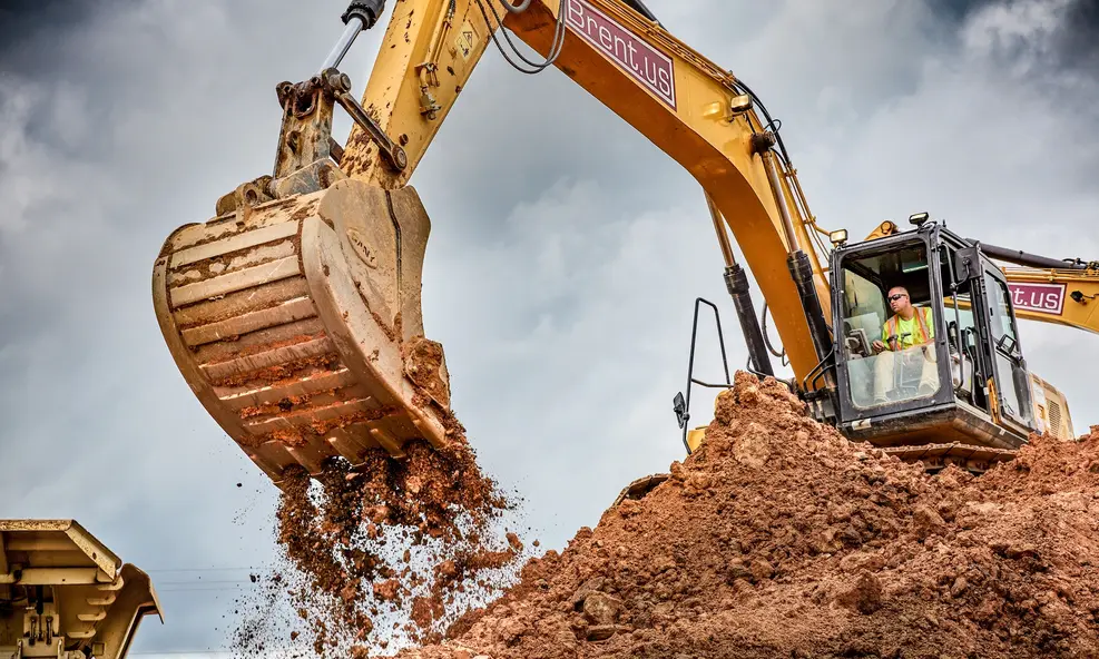 Excavator lifting and dumping red soil at a construction site with visible branding and dynamic movement.