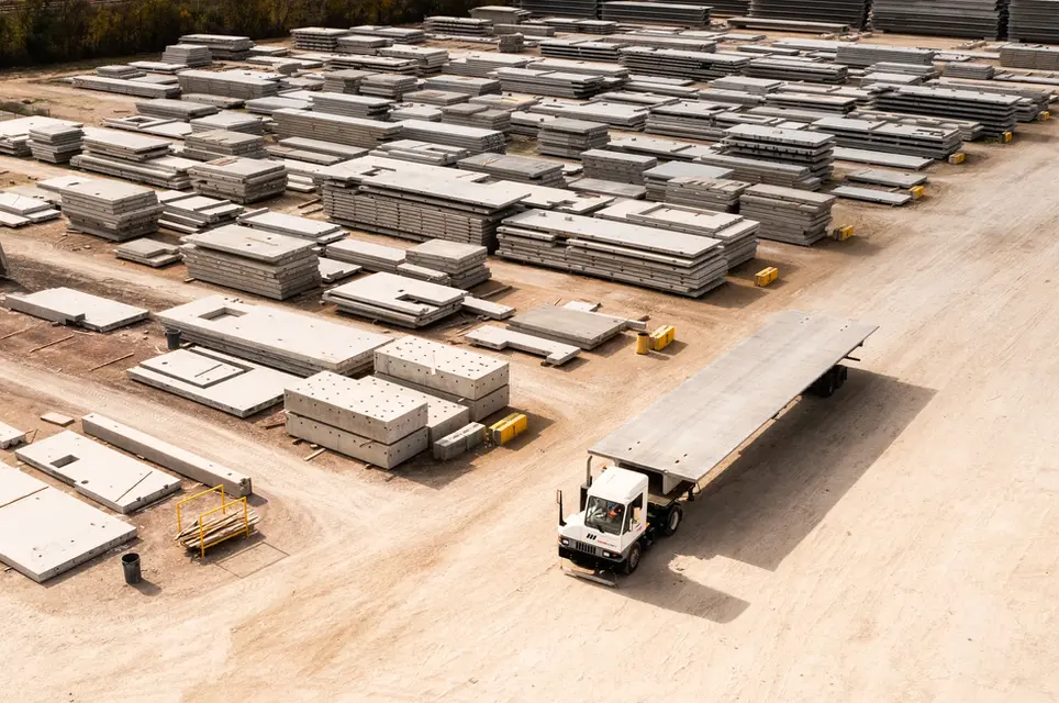 Drone aerial photography of a flatbed truck in a concrete panel yard with organized material stacks.