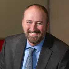 Corporate headshot photography of a smiling man with a beard in a gray suit jacket, light blue shirt, and paisley tie.