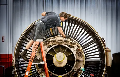 Technician servicing the interior of a jet engine with visible fan blades and tools.