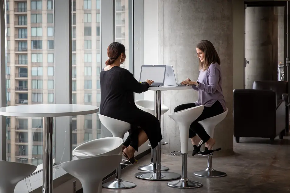 Women working at laptops by city windows reflect flexible work and modern design in corporate lifestyle offices.