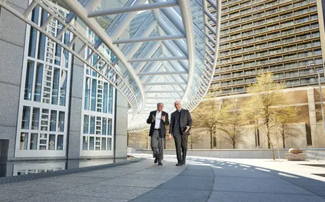 Professionals walk beneath a modern canopy, representing leadership presence in corporate lifestyle environments.