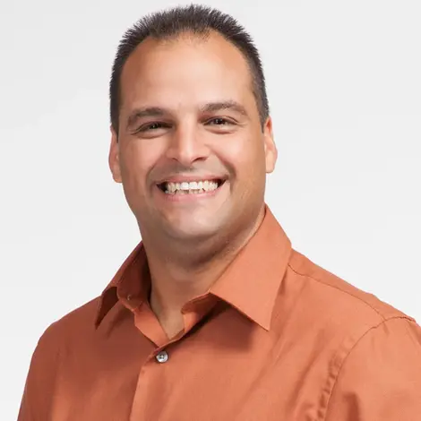 Corporate headshot photography of a smiling man in an orange dress shirt, standing against a white background.