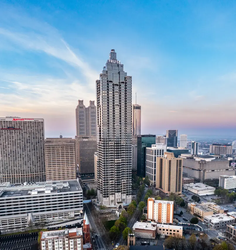 Drone photography services capturing a tall skyscraper among downtown buildings at sunset.
