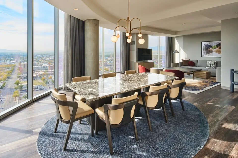 Modern hotel suite dining area with city view, marble table, and elegant seating.