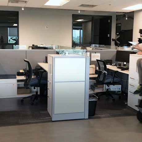 Motion blur image of office cubicles as a person rides past on a scooter, creating dynamic energy.