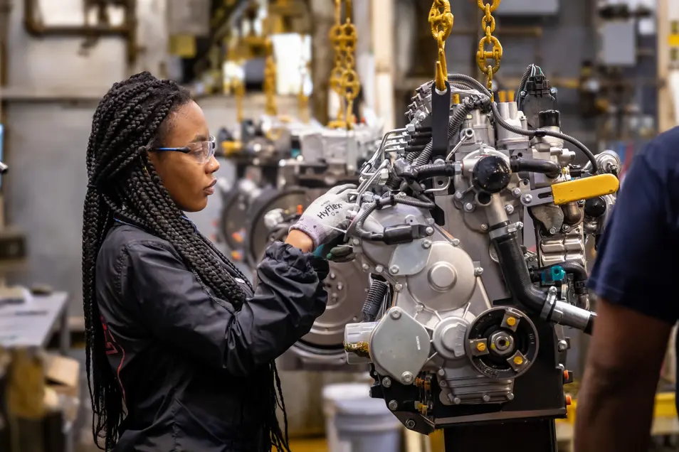 Female worker inspecting or assembling mechanical engine parts in factory.