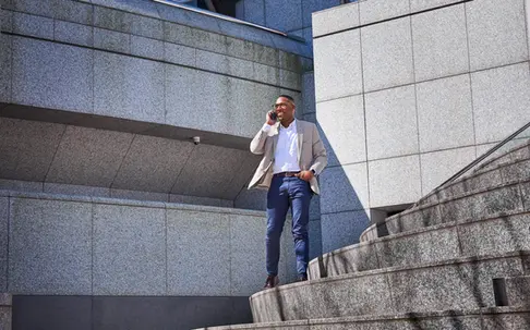 Man in blazer on phone stands confidently on city steps for lifestyle product photography.