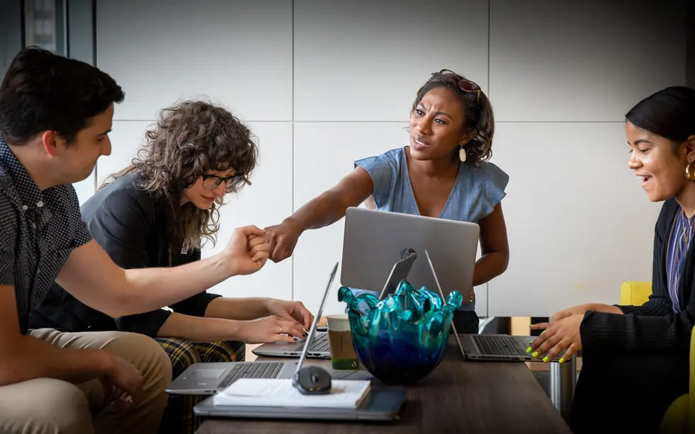 A coworker offers a fist bump during a brainstorm, reflecting camaraderie in corporate lifestyle collaboration.