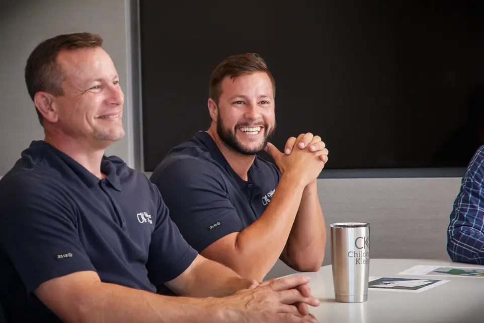 Coworkers in branded polos smile during a meeting, reflecting team pride in corporate lifestyle workplaces.