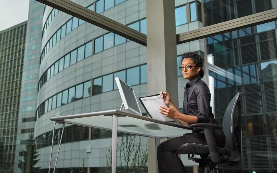 A focused woman reviews her planner at a desk with city views, reflecting productivity in corporate lifestyle offices.