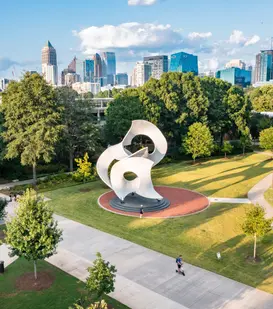 Aerial photography with drones showing a modern sculpture in a park with city skyline in background.