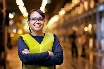 A professional business portrait of a factory worker in safety gear, smiling confidently on a production floor.
