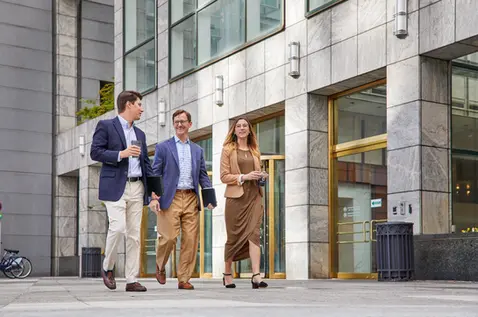 Professionals walk and talk outside an office building, showing mobility and connection in a corporate lifestyle setting.